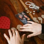 Close-up of hands arranging broken hearts near a couple's photo on a wooden table.