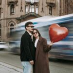 Romantic couple embracing with heart-shaped balloon in front of city street and blurred motion of vehicles.
